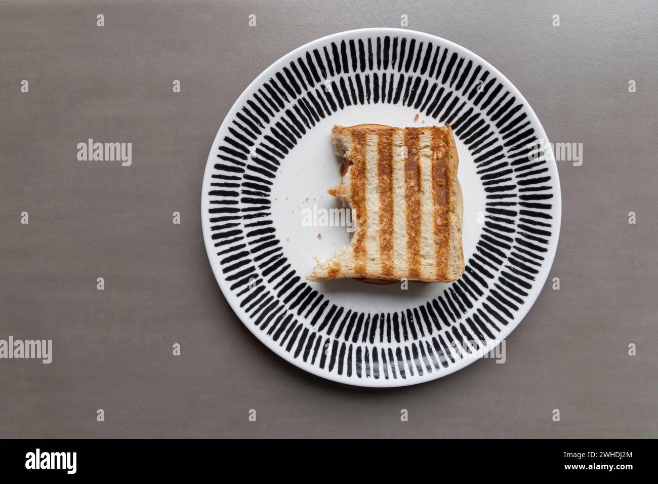 Ein Sandwich mit gegrilltem Schinken und Streifenmuster liegt auf einem Teller vor grauem Hintergrund Stockfoto