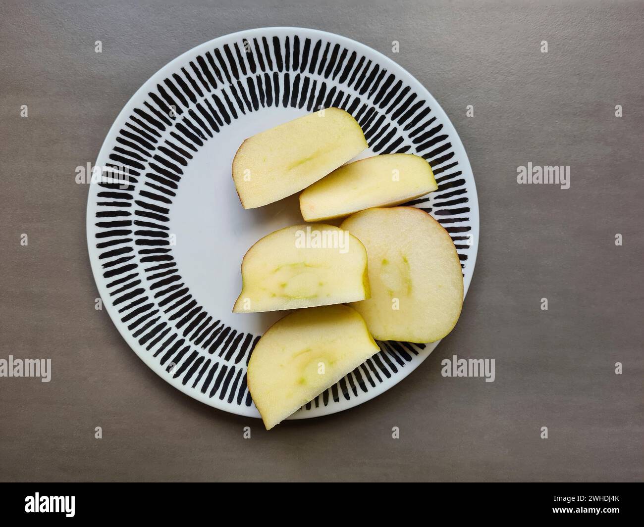 Ein frischer Apfel wird auf einem hellen Teller mit dunklem Hintergrund geschnitten Stockfoto