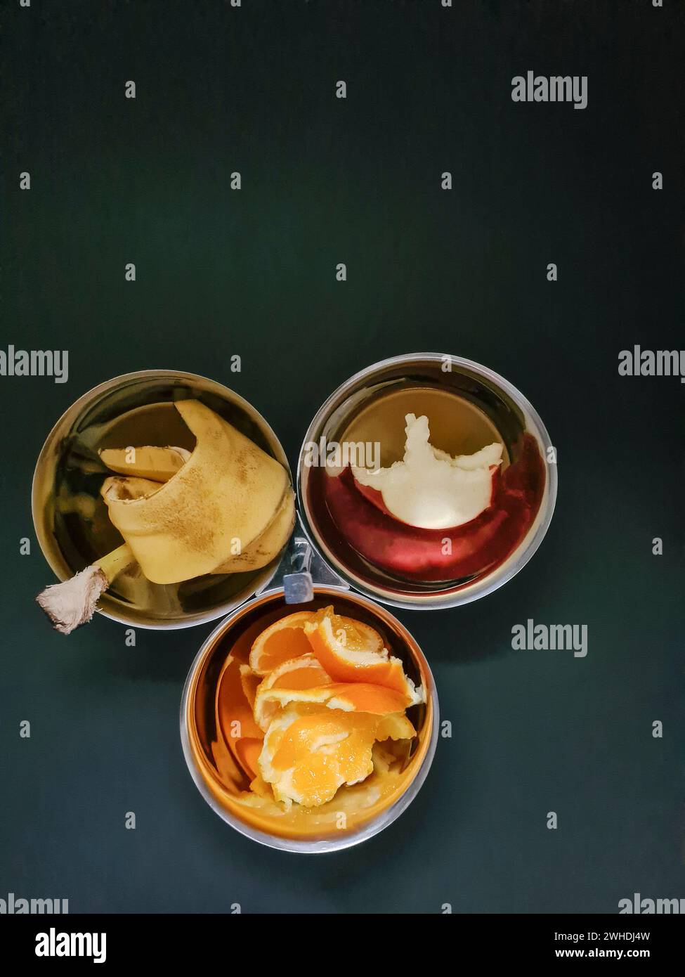 Gebissene Apfelscheibe, Bananenscheibe und Orangenschale in einer der drei Silberschalen vor grauem Hintergrund, Diät-Thema Stockfoto