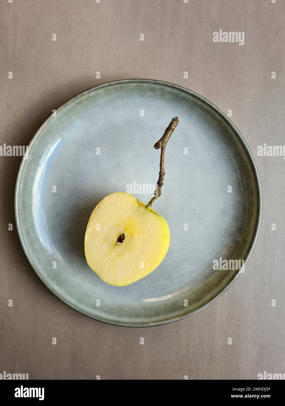 Ein frischer halbierter Apfel mit Kern liegt auf einem pastellfarbenen Teller und hellgrauem Hintergrund Stockfoto