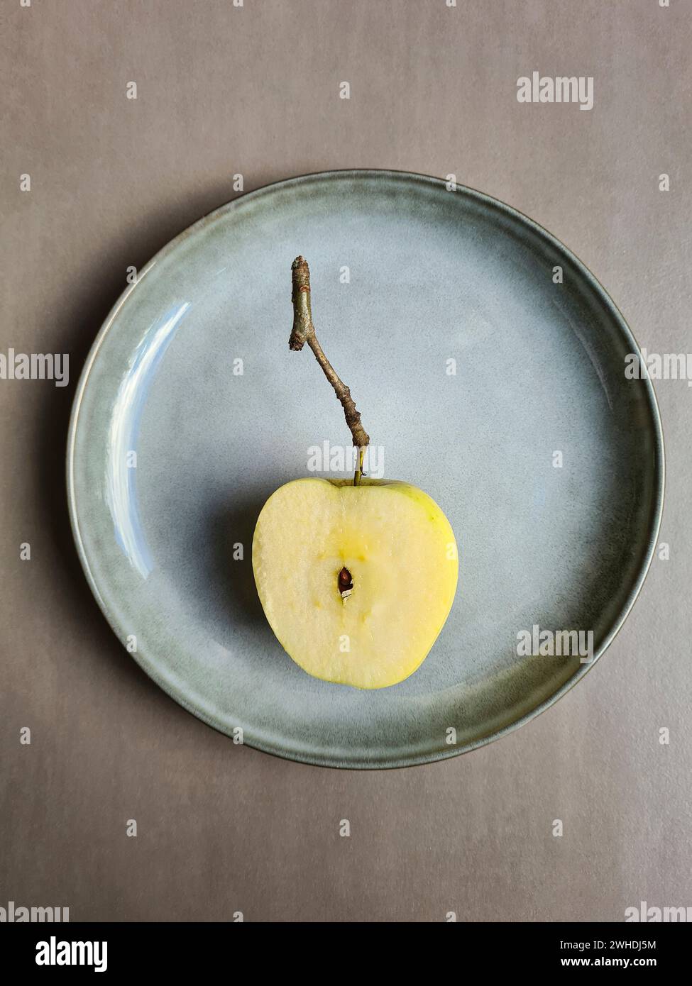 Ein frischer halbierter Apfel mit Kern liegt auf einem pastellfarbenen Teller und hellgrauem Hintergrund Stockfoto