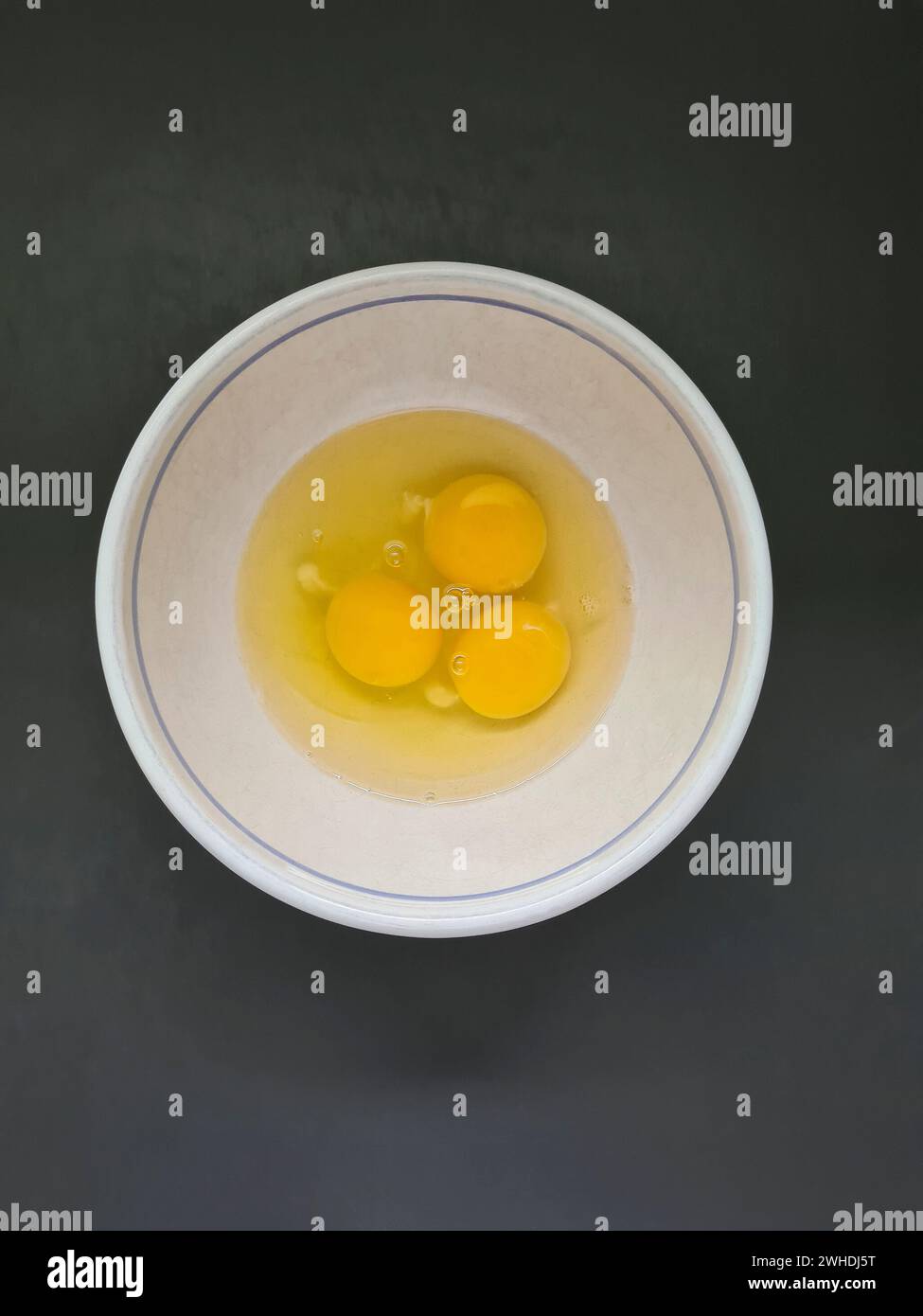 Drei verprügelte rohe Eier, Eiweiß und Eigelb in einer weißen Schüssel Stockfoto