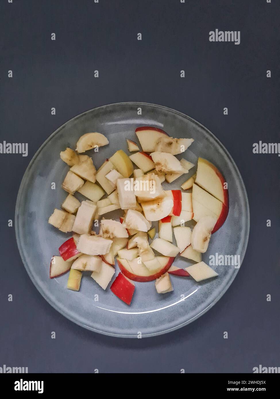 Apfelstücke mit roter Apfelhaut, in kleine Stücke geschnitten als Obstsalat auf einer hellblauen Platte Stockfoto