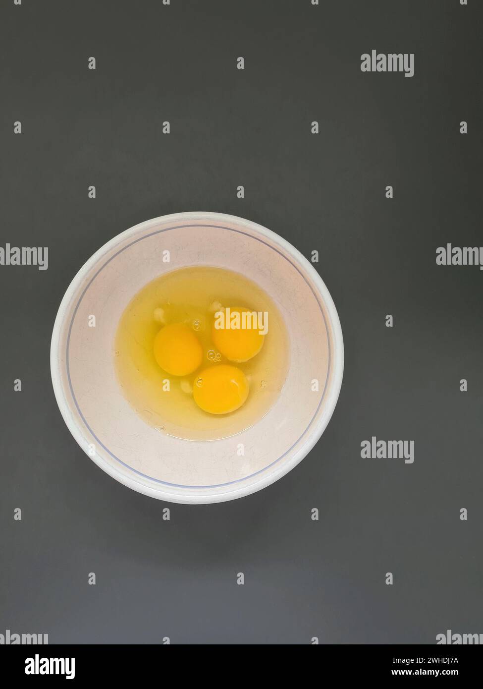 Drei verprügelte rohe Eier, Eiweiß und Eigelb in einer weißen Schüssel Stockfoto