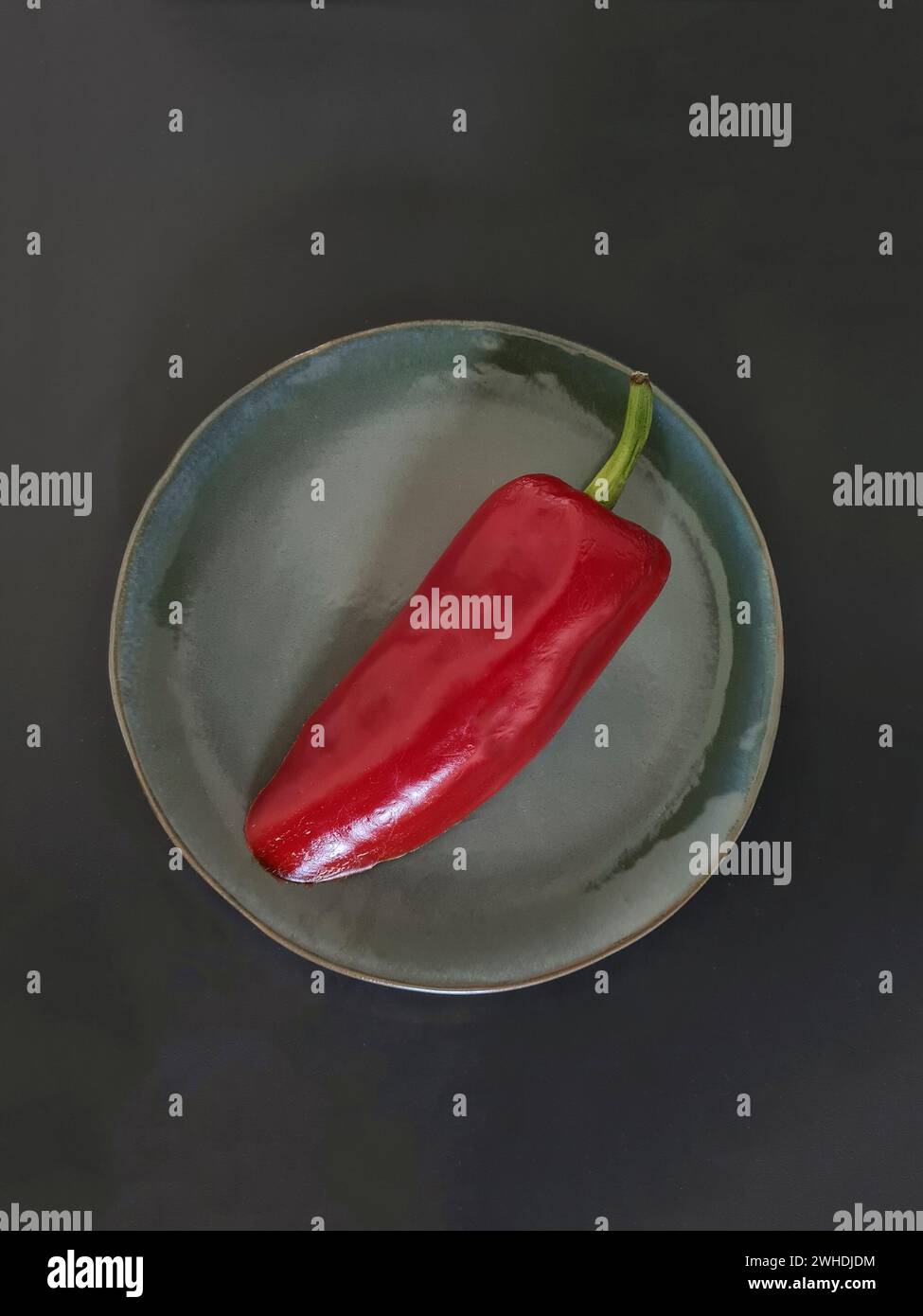 Eine rote Paprika mit grünem Stiel liegt auf einer grünen Platte Stockfoto