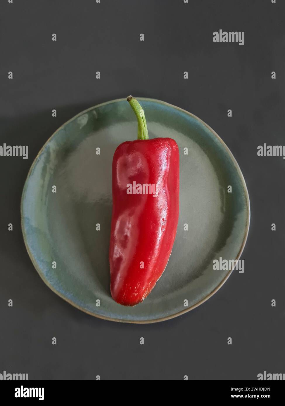 Eine rote Paprika mit grünem Stiel liegt auf einer grünen Platte Stockfoto