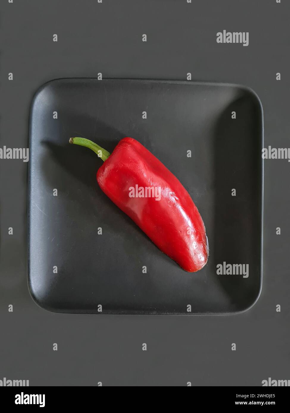 Eine rote Paprika mit grünem Stiel liegt auf einer schwarzen Platte Stockfoto