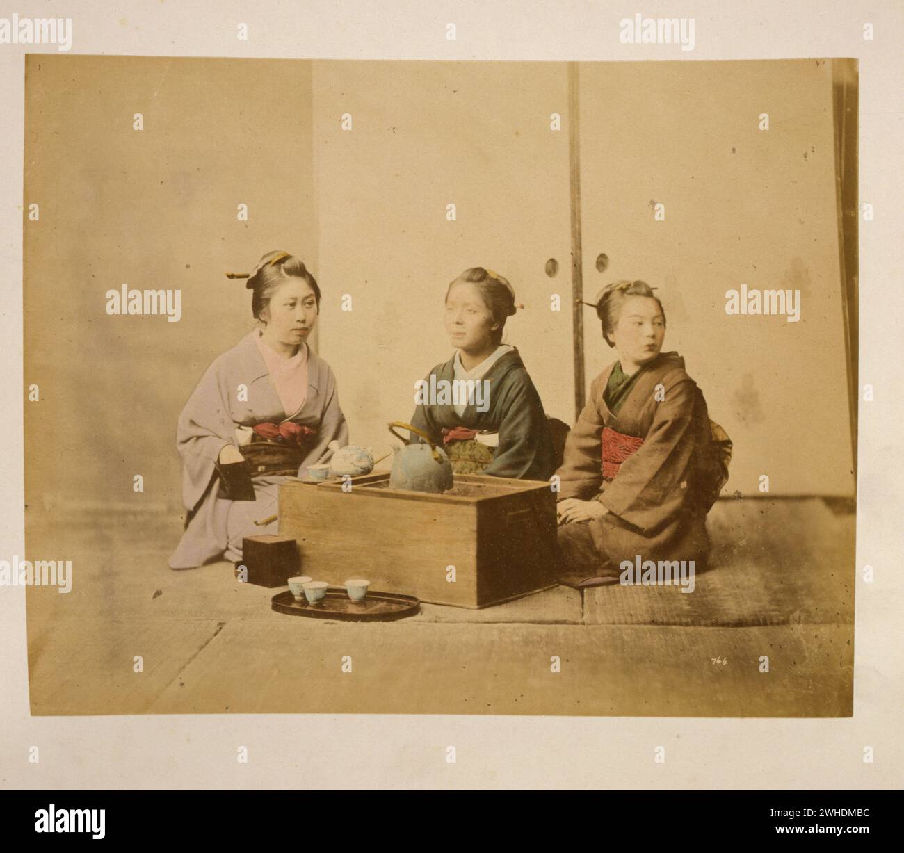 Drei Frauen, die auf dem Boden um einen Holztisch sitzen, sitzen Tee... Japan handkoloriert mit Aquarellbildern um die 1870er Jahre Stockfoto