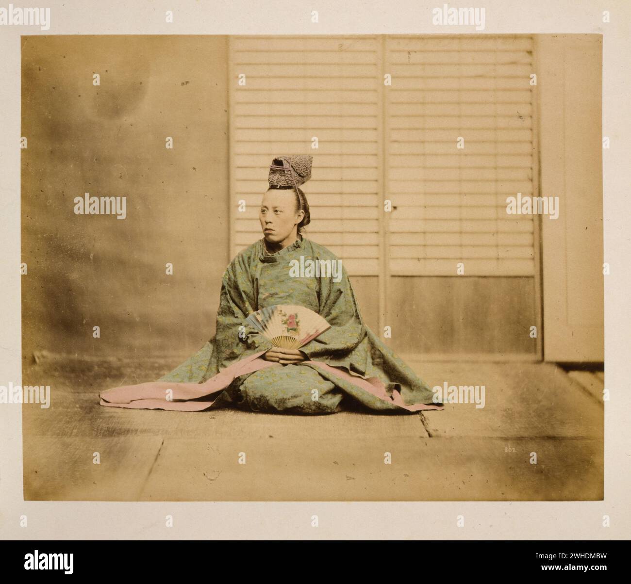 Ein Mann, möglicherweise ein Regierungsbeamter, der einen Ventilator in der Hand hält, sitzend, nach links gerichtet, mit einem kronenähnlichen Hut... Japan handbemalt mit Aquarellbild um 1870er Jahre Stockfoto