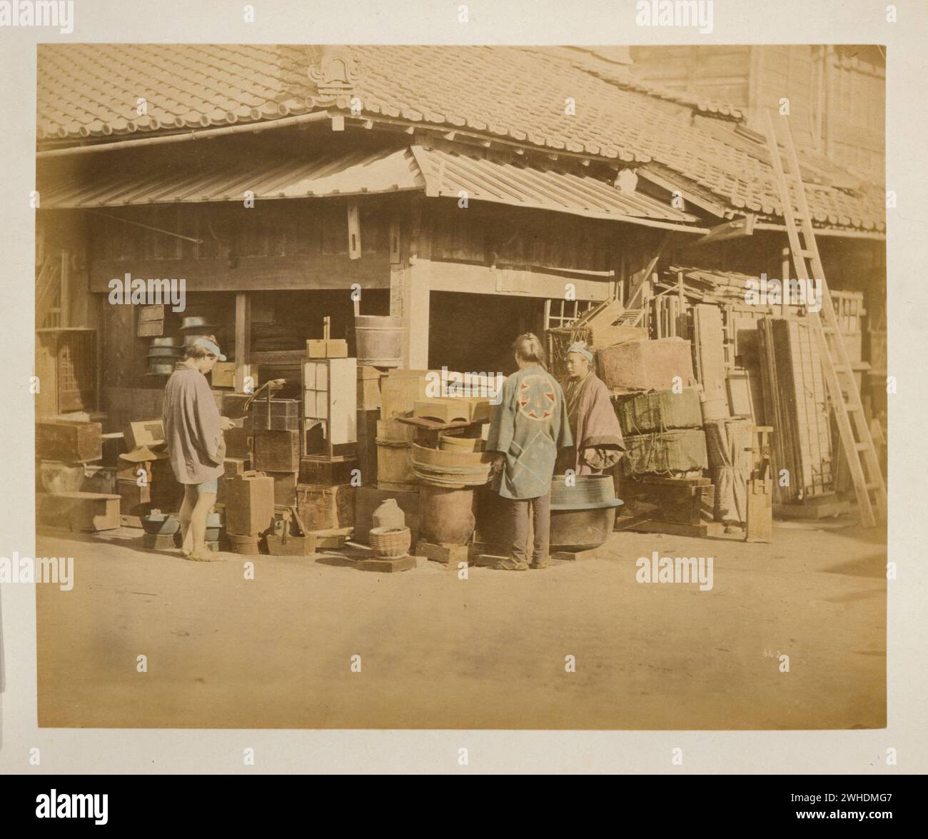 Außenansicht des Ladens an der Straßenecke mit Waren entlang der Straßenränder und drei Personen, Einkäufer und Händler... Japan handkoloriert mit Aquarell-Fotografie um die 1870er Jahre Stockfoto