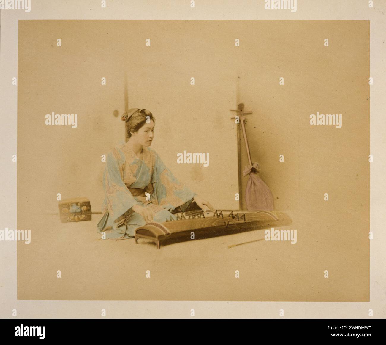 Japanische Frau, in voller Länge, sitzend, nach rechts gerichtet, Koto spielt; ein Schamisen lehnt sich an eine Wand im Hintergrund... Japan handkoloriert mit Aquarell Fotografie Print um 1870er Jahre Stockfoto