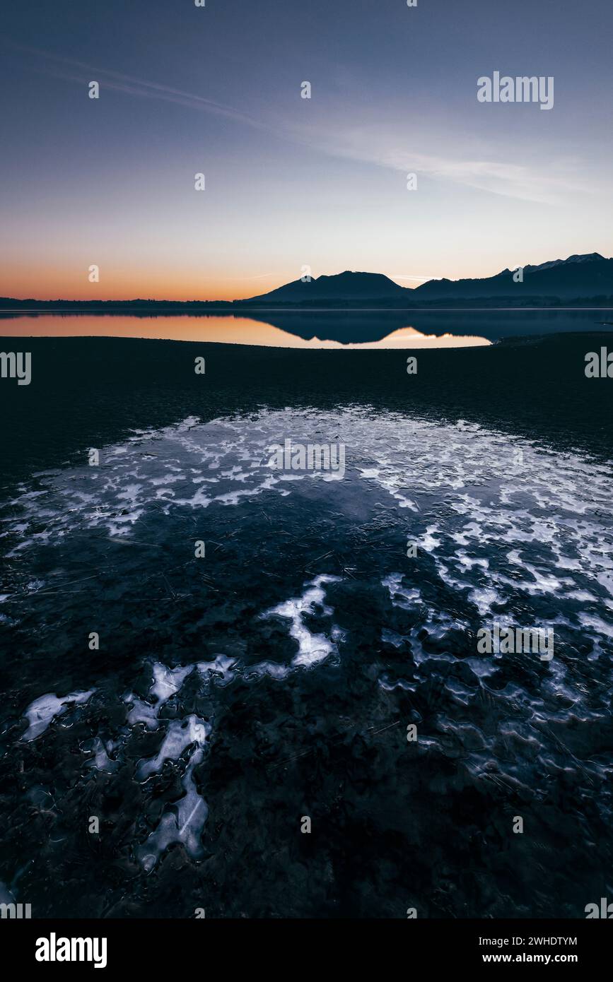 Sonnenaufgang im entwässerten Forggensee bei Füssen mit Eis im Vordergrund Stockfoto