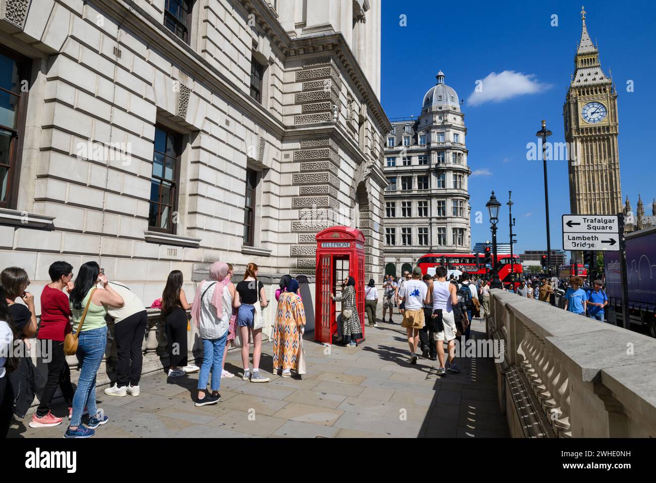 Touristen stehen an, um ein Foto mit der berühmten roten K2-Telefonbox zu machen, mit Big Ben im Hintergrund Parliament Square, London, Großbritannien. August 2023 Stockfoto