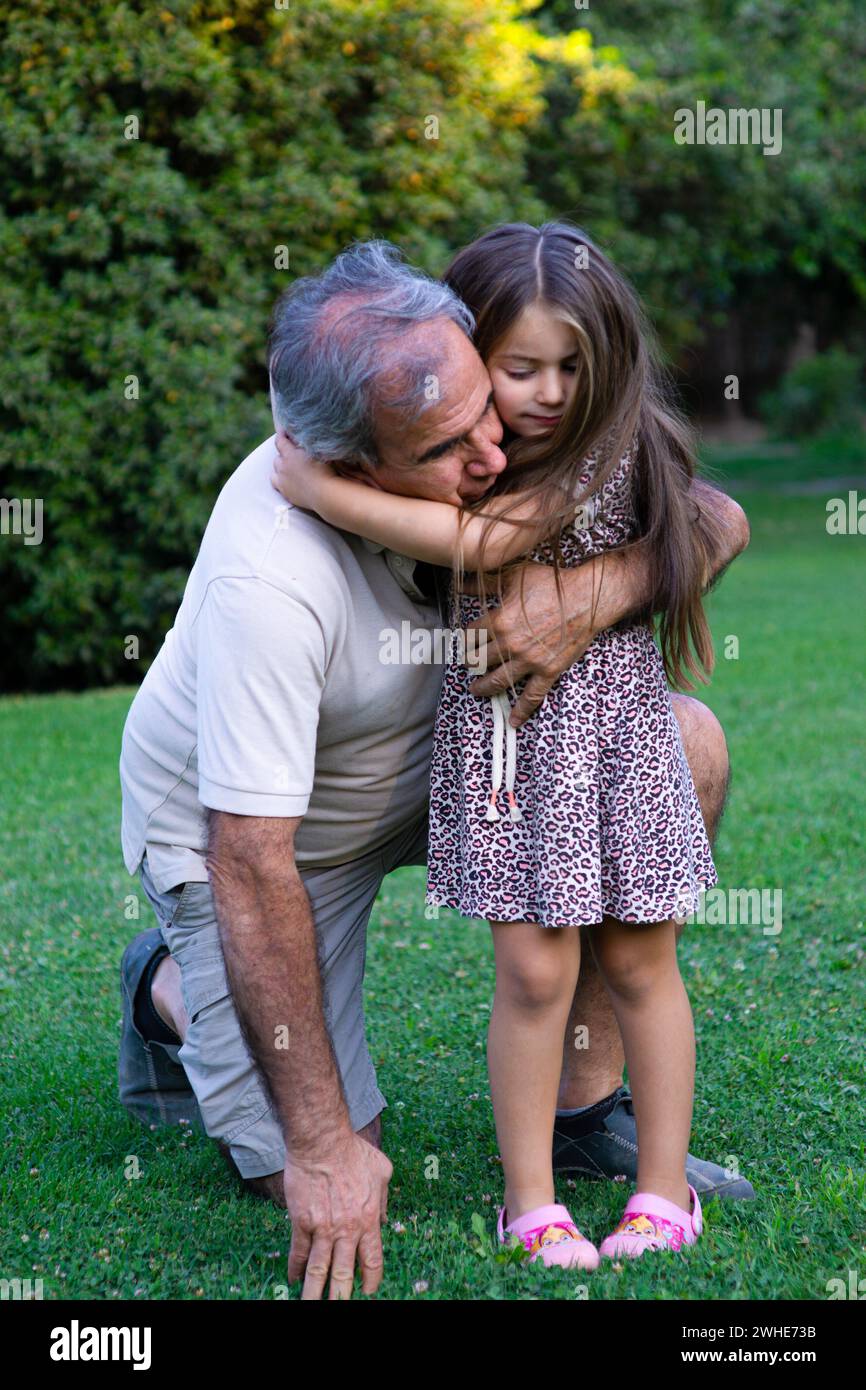 Abuelo y nieta compartiendo momentos speciales bajo la sombra de los árboles, una escena llena de sonrisas, amor y la belleza del campo en verano Stockfoto