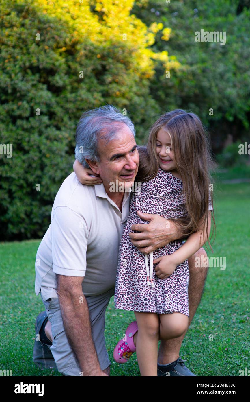 Abuelo y nieta compartiendo momentos speciales bajo la sombra de los árboles, una escena llena de sonrisas, amor y la belleza del campo en verano Stockfoto