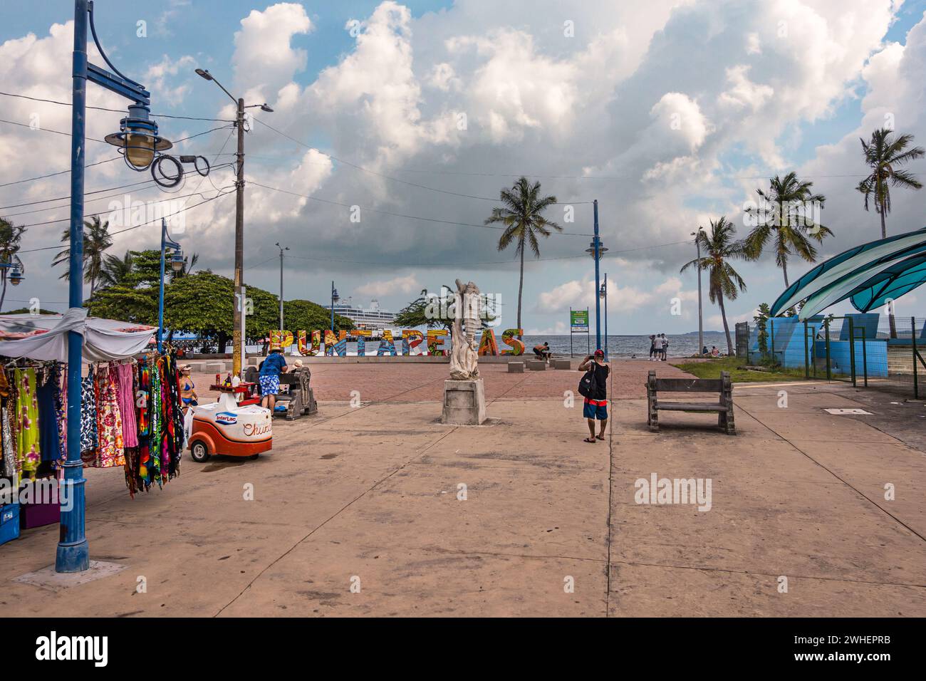 Costa Rica, Puntarenas - 22. Juli, 20.23: Platz am Anfiteatro Cultural La Concha Acústica. Straßenverkäufer und Textilladen. Schiff auf Pier hinter Green Stockfoto