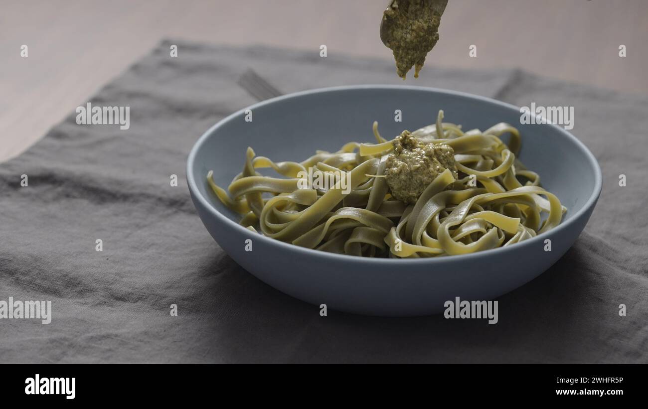 Pesto zu grüner Fettuccine in blauer Schale geben, breites Foto Stockfoto