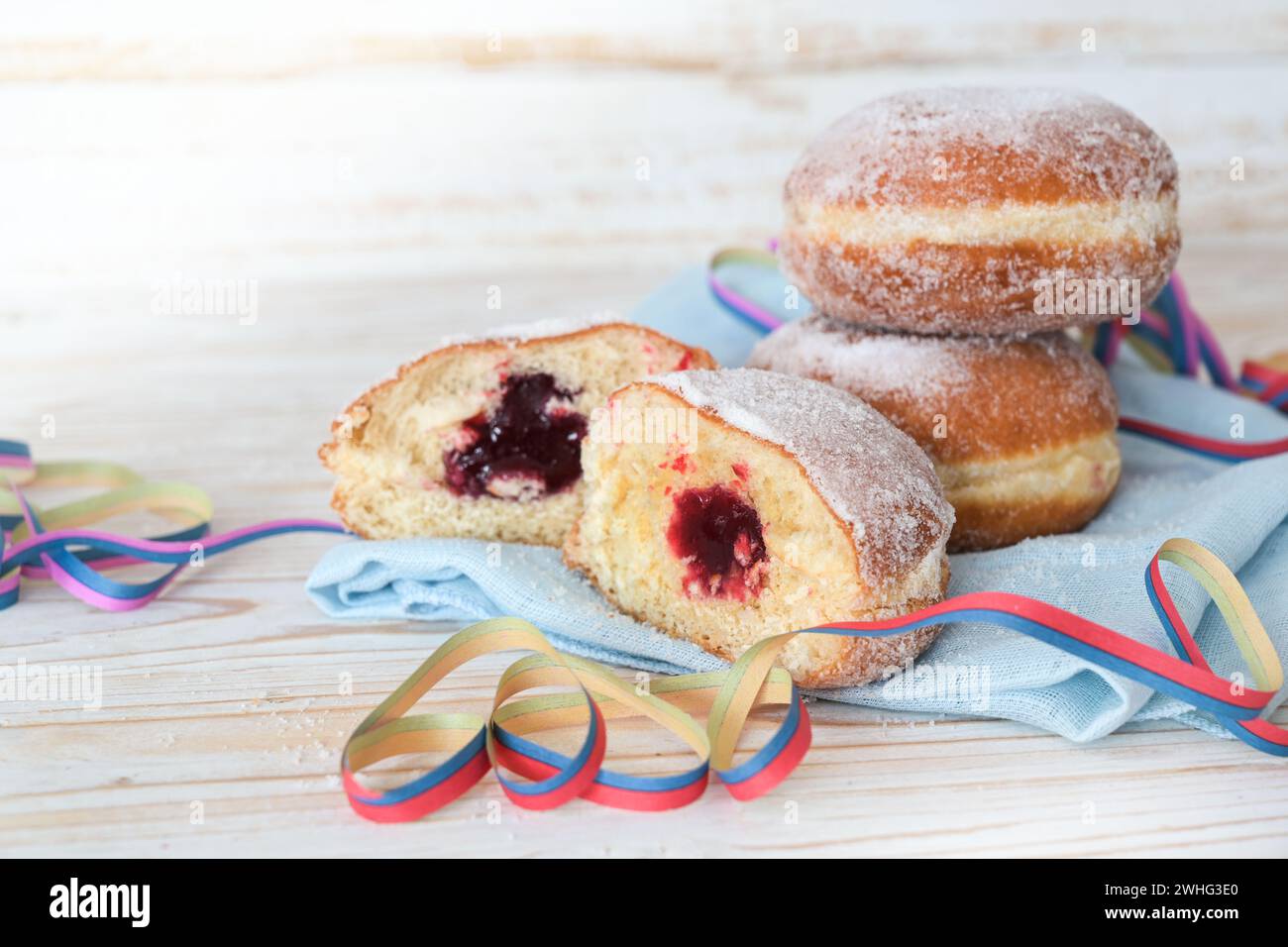 Berliner Donuts, auch Krapfen genannt, gefüllt mit Marmelade auf einer Serviette mit Party-Streamer, süßem Gebäck für Fasching und Silvester, li Stockfoto