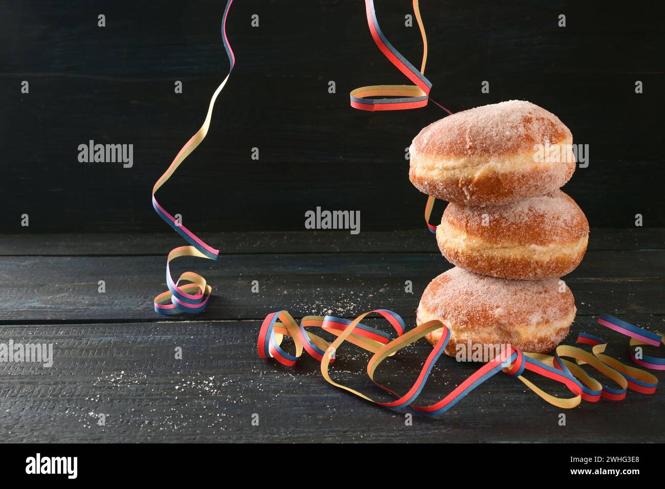 Gestapelte Berliner Donuts oder Krapfen und einige Party-Streamer vor dunklem rustikalem Hintergrund, oft an Neujahr und ca. Stockfoto