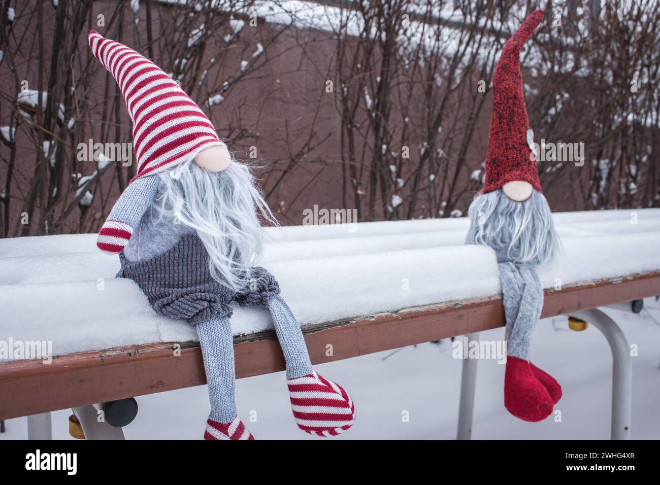 Ein paar Zwerge auf der Bank im Schnee. Romantisches Geschenk. Freundschaftskonzept. Valentinstag-Konzept. Gnome mit Herz und rotem Hut im Schnee. Stockfoto