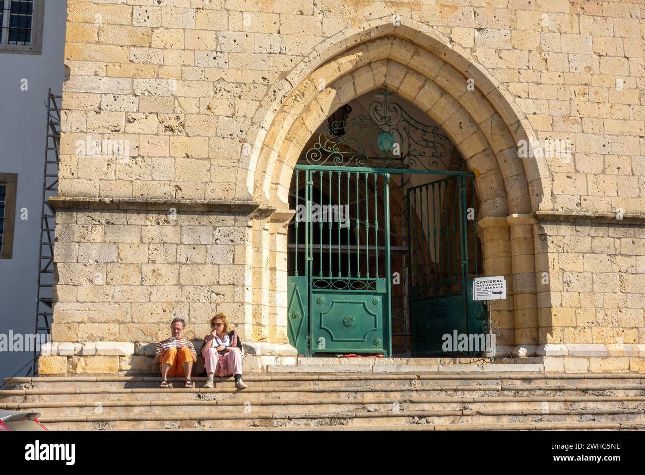 Touristen-Paar Mann Und Frau Sitzen Auf Den Stufen Der Kathedrale Von Faro, Der Algarve Portugal 6. Februar 2024 Stockfoto