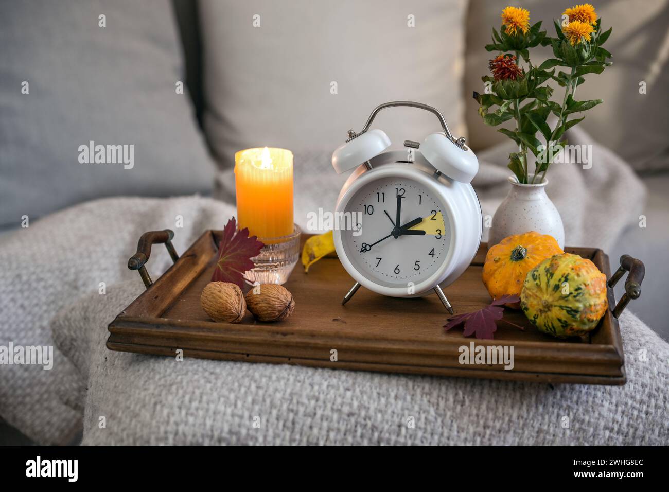 Vintage-Wecker, der eine Stunde nach der Sommerzeit zurückfällt, Holztablett mit Kerze und Herbstdekoration auf einem Be Stockfoto