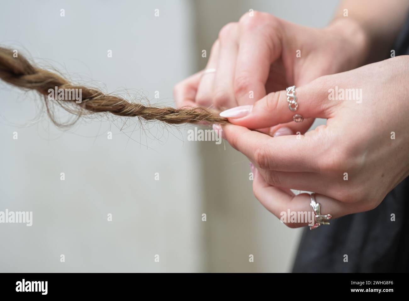 Hände einer jungen Frau mit Ringen und gestylten Nägeln, die das Haar eines Freundes flechten, Kopierraum, ausgewählter Fokus Stockfoto