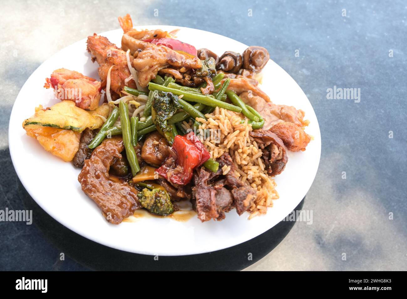 Verschiedene chinesische Fleisch- und Gemüsesorten mit gebratenem Reis auf einem weißen Teller und einem blauen Tisch, Kopierraum, ausgewählter Fokus Stockfoto