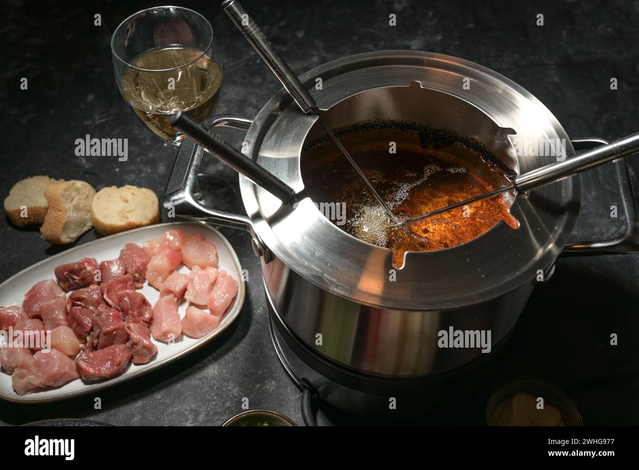 Fonduekanne mit kochendem heißem Öl, langen Gabeln und rohem Fleisch, Partydinner für Freunde und Familie, ausgewählter Fokus Stockfoto