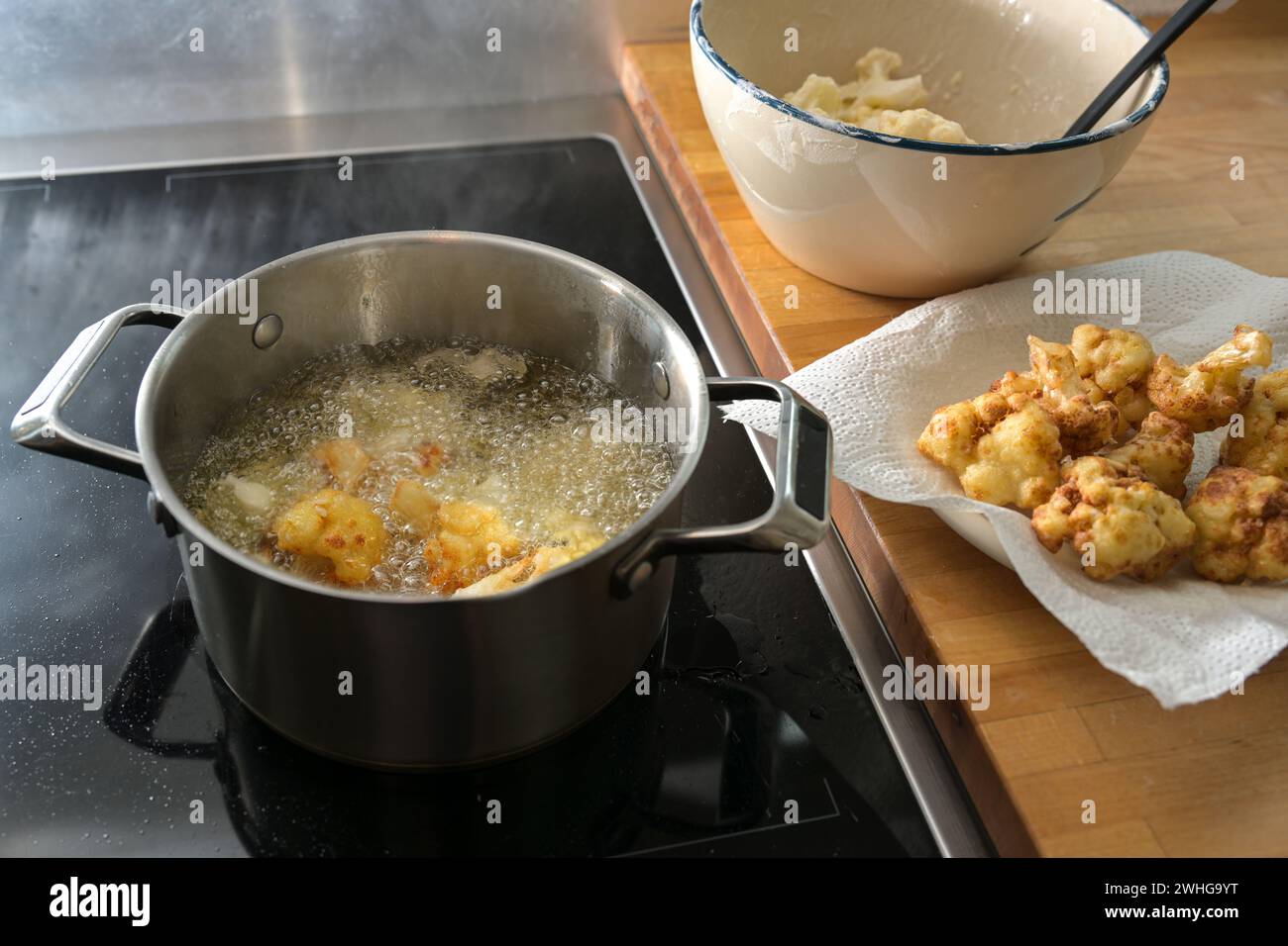 Frittierter Blumenkohl in der Verarbeitung, in heißem Speiseöl in einem Topf braten, auf einem Papiertuch trocknen und roh in einer Schüssel, Zubereitung von Stockfoto