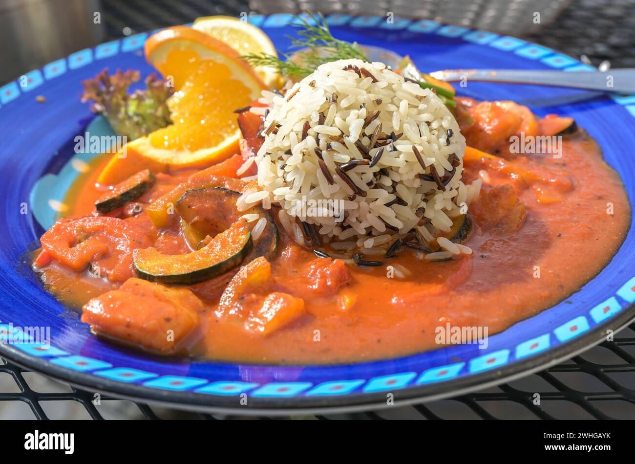 Scharfe Tomatensauce mit Gemüse und Fisch serviert mit weißem und schwarzem Reis auf einer blauen Platte, ausgewählter Fokus Stockfoto