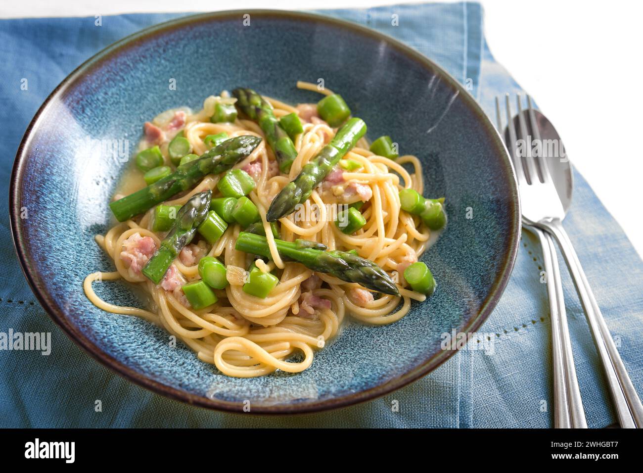 Spaghetti Carbonara mit grünem Spargel auf blauem Teller mit Serviette und Besteck, ausgewählter Fokus Stockfoto