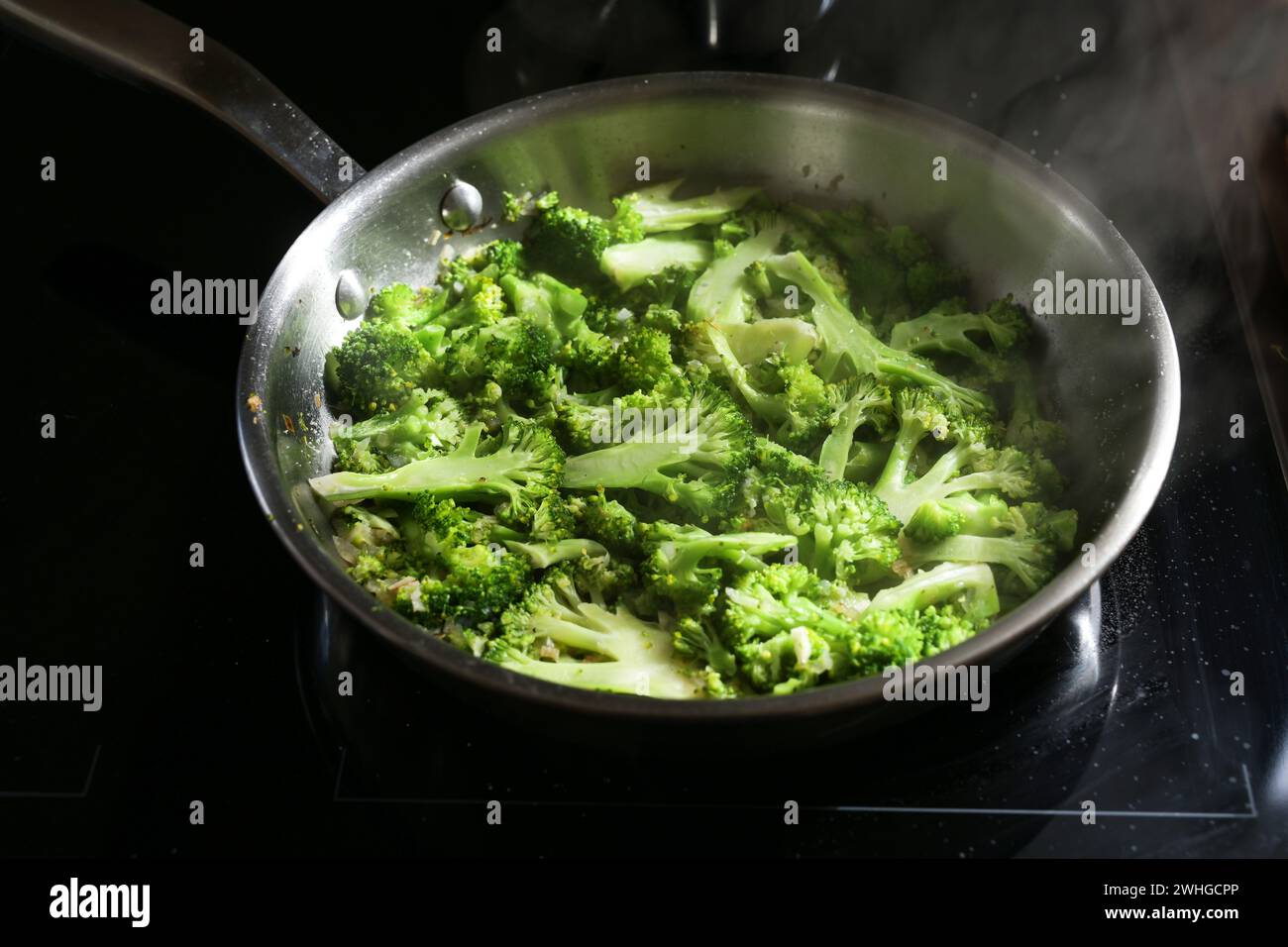 Brokkoli in Scheiben in einer Edelstahlpfanne auf schwarzem Herd, gesundes Kochen mit frischem Gemüse, ausgewählter Fokus Stockfoto