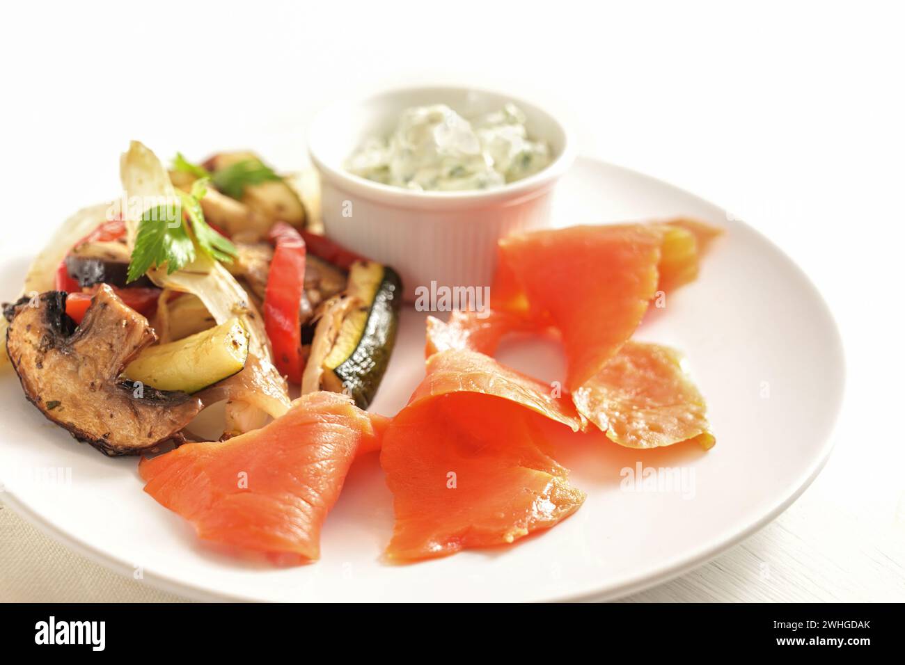Geräucherter Lachs mit Gemüse und Dip auf einem weißen Teller, gesunder Snack mit niedrigen Kalorien für eine Schlankheitsdiät, ausgewählter Fokus Stockfoto