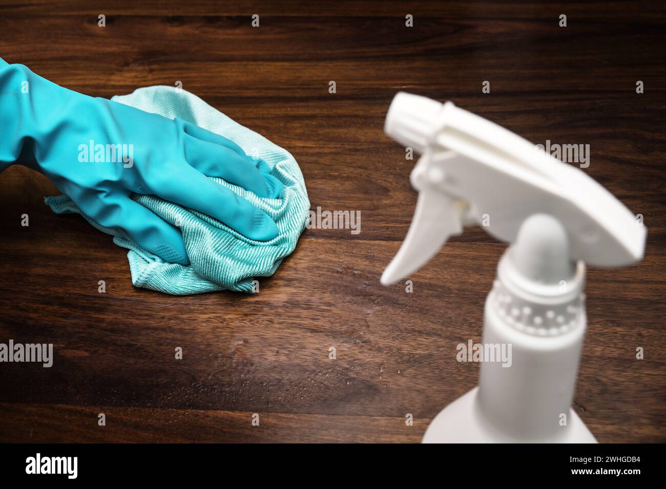 Oberflächendesinfektion gegen Coronavirus-Ausbreitung, Hand mit blauem Gummihandschuh reinigen einen dunklen Holztisch, weiße Flasche mit Stockfoto