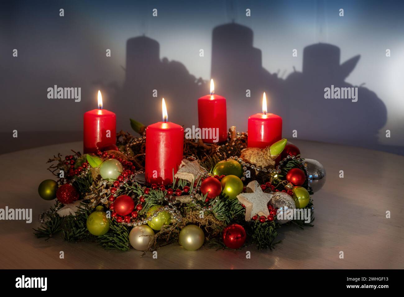 Adventskranz mit roten und grünen Weihnachtskugeln, vier brennenden Kerzen und einem Schatten an der Wand, Kopierraum, ausgewählter Fokus Stockfoto