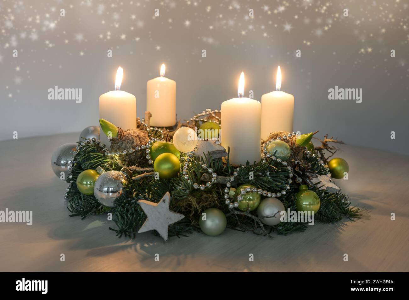 Vierter Adventskranz mit vier brennenden weißen Kerzen und grüner Weihnachtsdekoration auf einem Tisch, Wohnkultur für die vierte Sunda Stockfoto