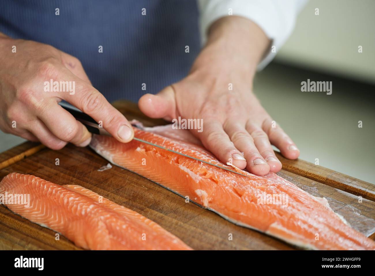 Saibfisch filetieren, Hände des Kochs entfernen die Knochen mit einem dünnen Filemesser auf einem Schneidebrett, ausgewählter Fokus Stockfoto