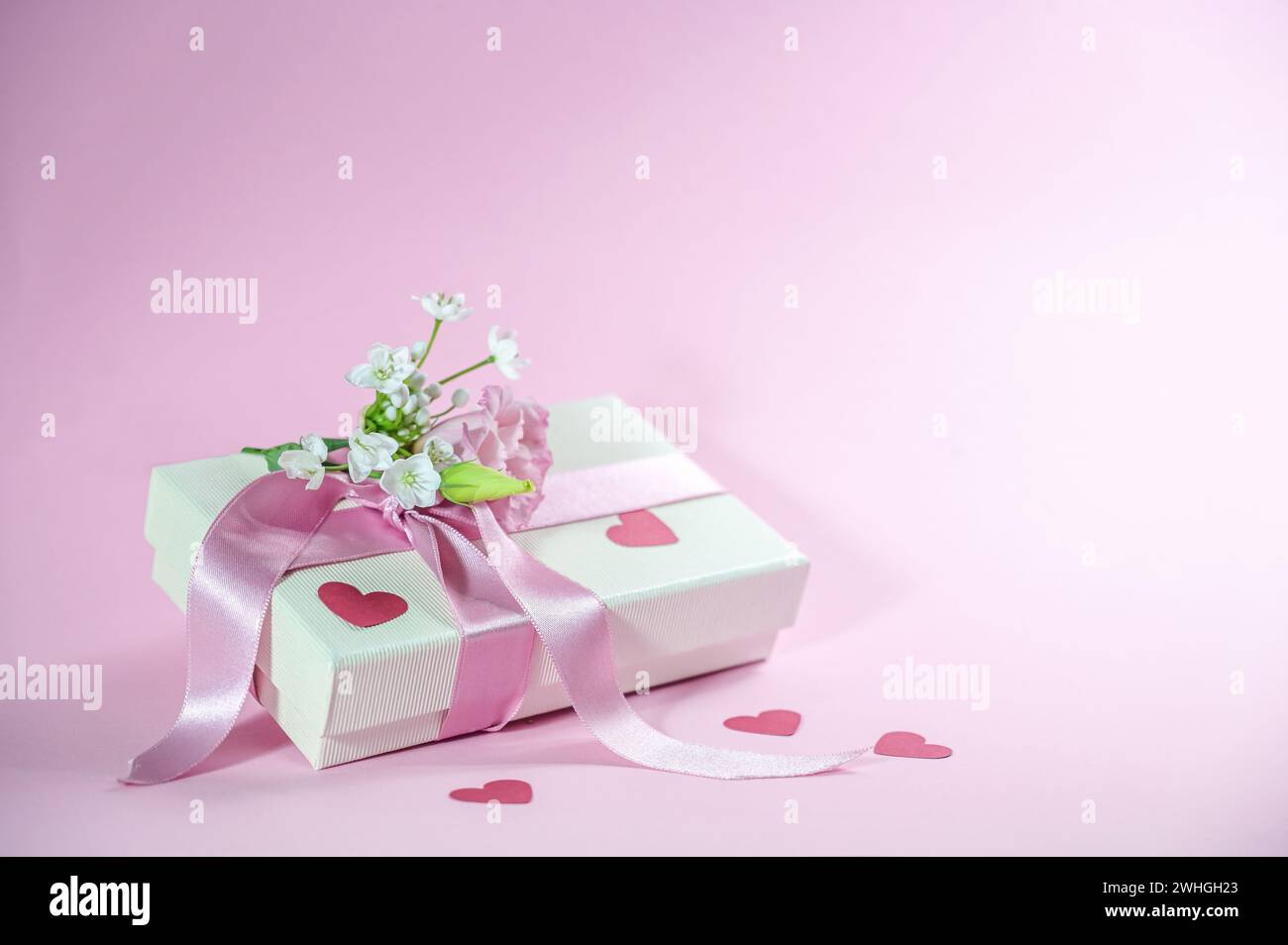 Geschenkbox mit Blumenstrauß, Band und Papier Herzformen auf einem hellrosa Hintergrund, Liebesgrußkarte zum Valentinstag, M Stockfoto