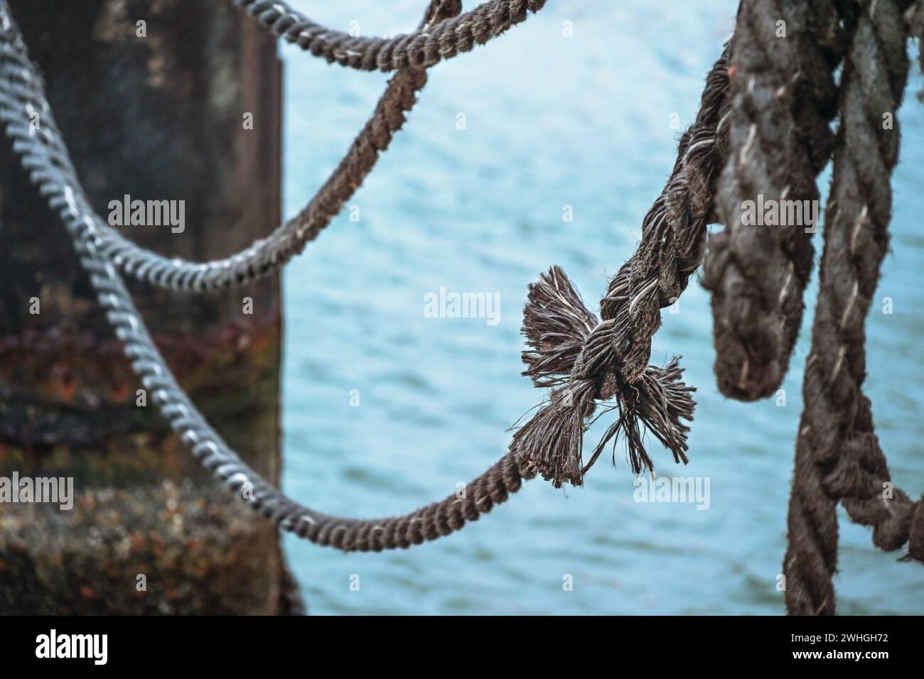 Knoten an einem alten Schiffseil auf einem Steg über dem Wasser, Metapher für Zusammenhalt, Kopierraum, ausgewählter Fokus Stockfoto
