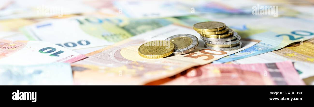 Münzstapel auf Euro-Banknoten im breiten Panoramaformat, Kopfzeilenkonzept für Unternehmen, Finanzen oder Inflation, Kopierraum Stockfoto