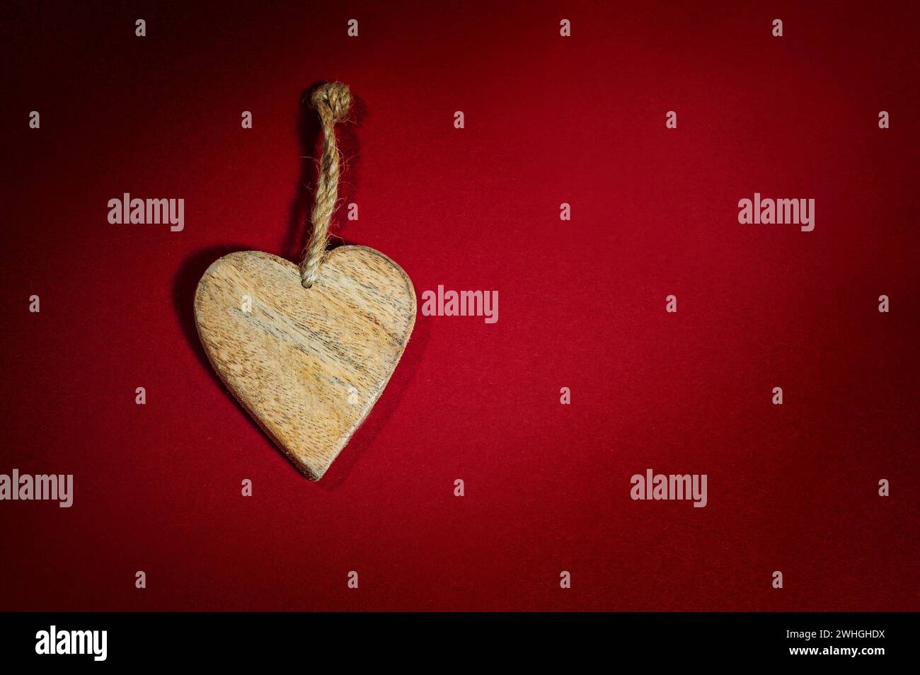 Einfache Herzform aus Holz mit rustikaler Kordelzug auf einem Hintergrund aus dunkelrotem Filz, Weihnachtsgrußkarte und Liebessymbol für V Stockfoto