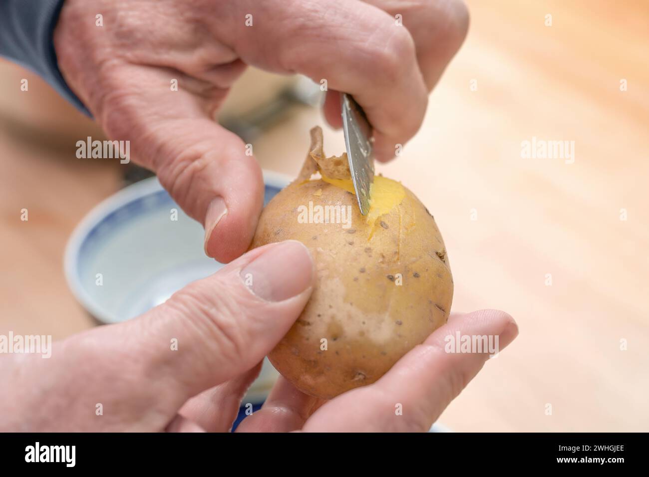 Hände eines älteren Mannes, der eine gekochte Kartoffel mit einem Küchenmesser schält, Lebensmittel zubereitet, Kopierraum, ausgewählter Fokus Stockfoto