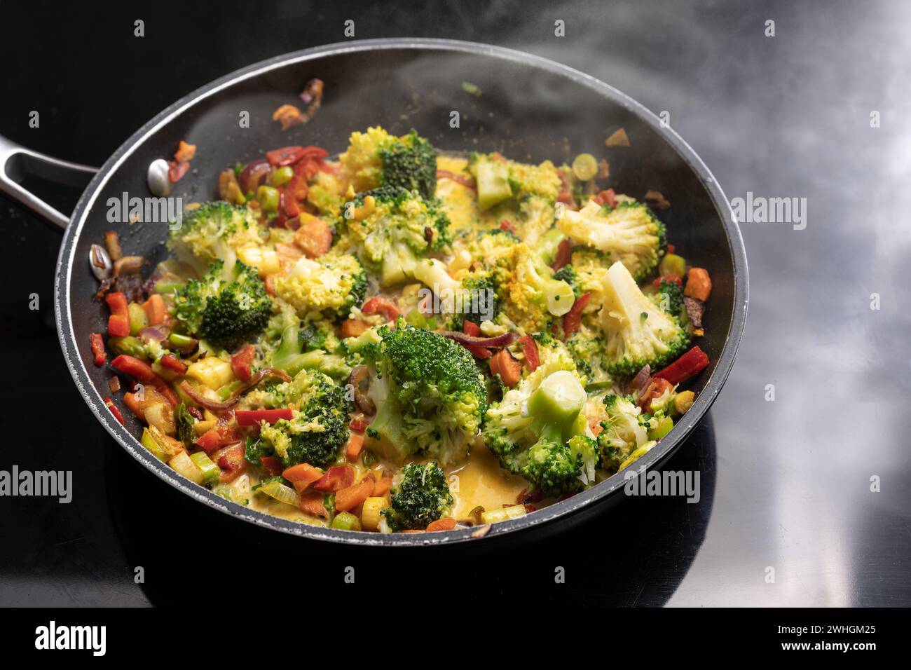 Vegetarisches Curry mit Brokkoli und anderem Gemüse in einer dampfenden Pfanne auf schwarzem Herd, asiatisches Kochkonzept, Copy sp Stockfoto