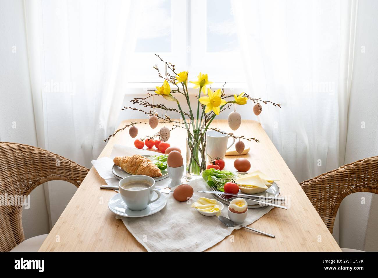 Frühstück für zwei Personen mit Narzissen und Osterdekoration auf einem Holztisch am Fenster, Kopierraum, ausgewählter Fokus Stockfoto