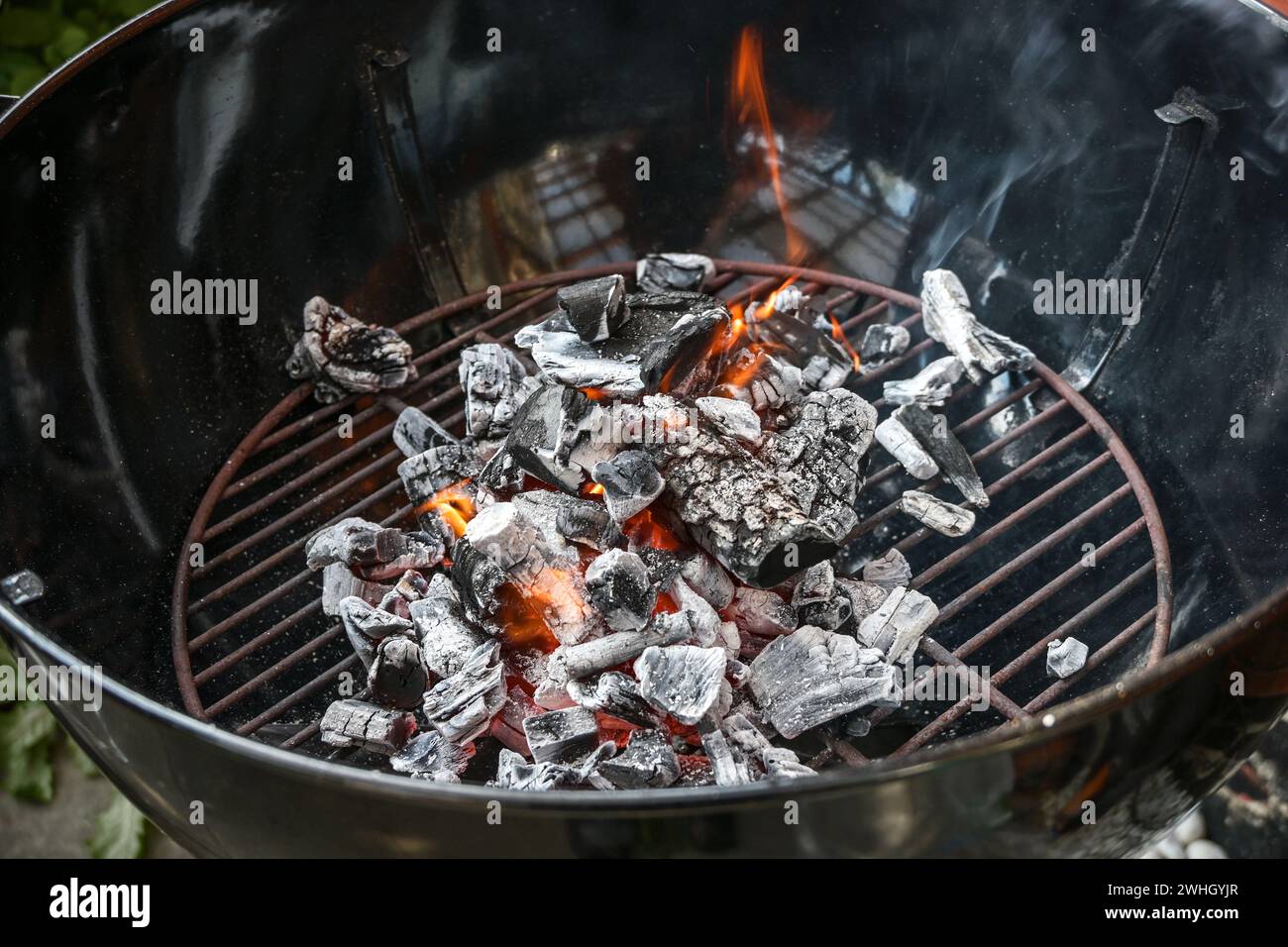 Mobiler runder Grill mit glühender Holzkohle, kleinen Flammen und Rauch, Vorbereitung auf eine Grillparty, Kopierraum, ausgewählter Fokus Stockfoto