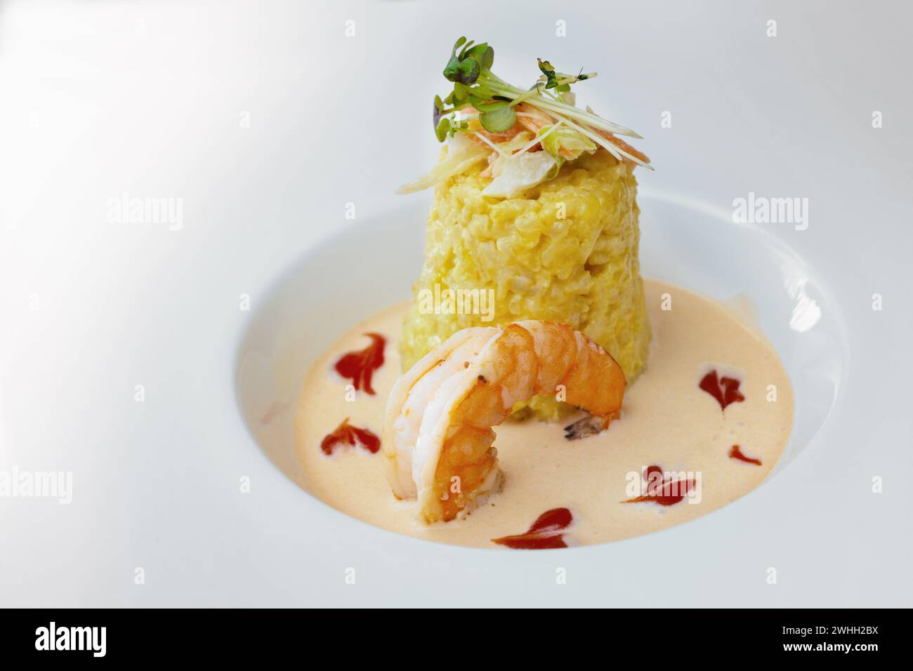 Gourmet-Gericht aus Safranrisotto mit Gemüse- und Kräuterbelag, einer großen Garnelen- und Krustentiersauce auf einer modernen weißen Platte, c Stockfoto