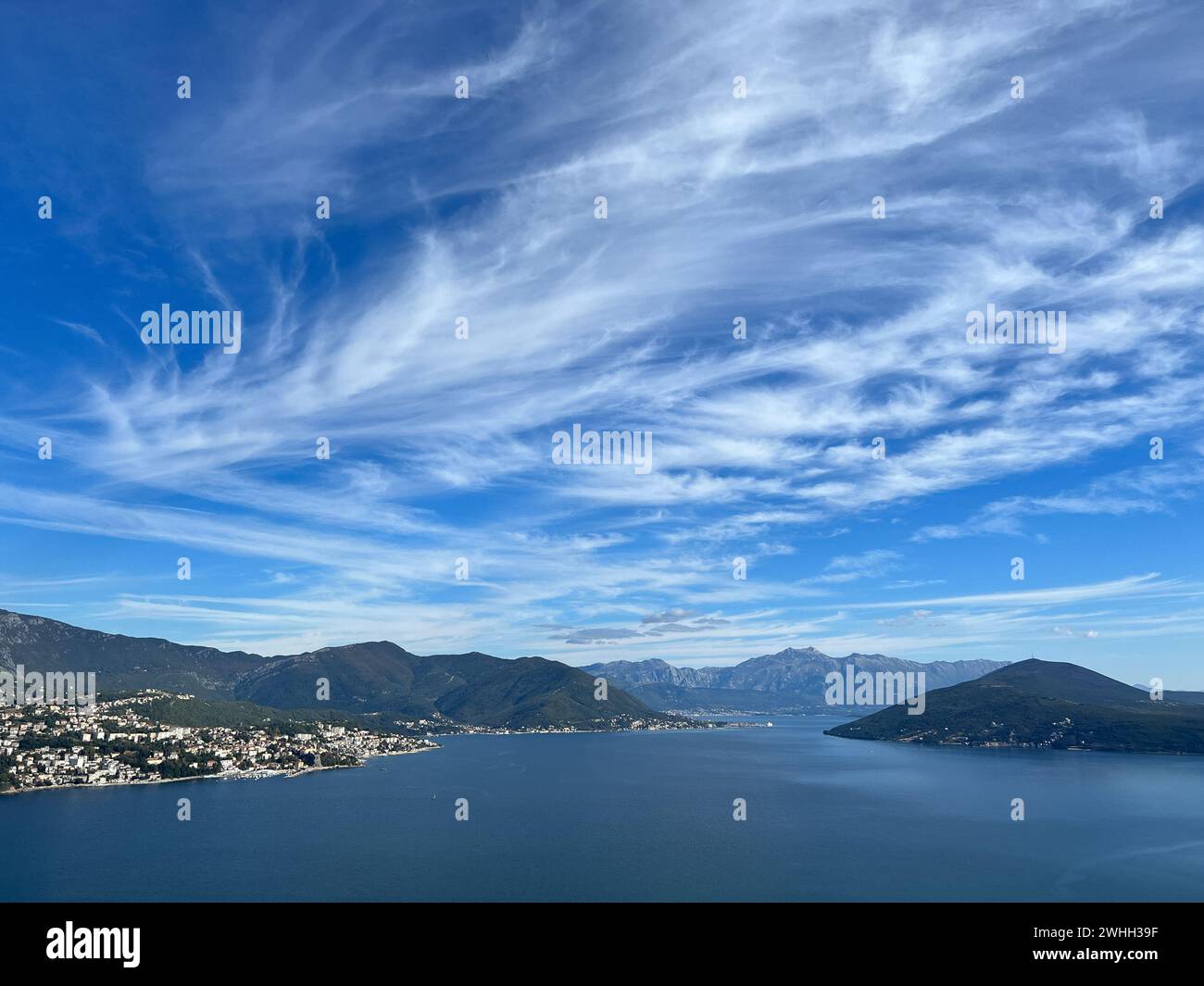 Weiße Zirruswolken am blauen Himmel über einem Gebirgszug in der Nähe des Meeres Stockfoto