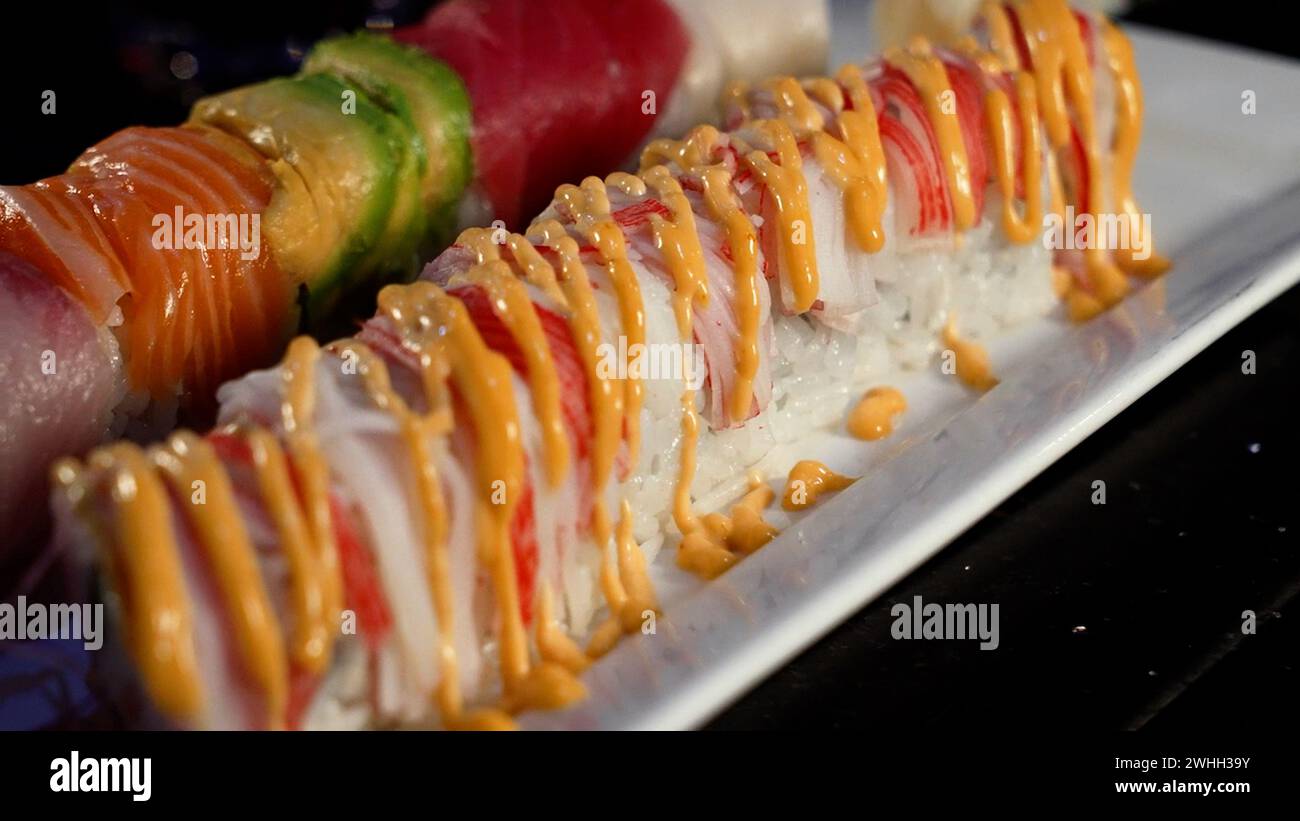 Verschiedene Sushi-Brötchen auf weißem Teller mit goldener Sauce Stockfoto