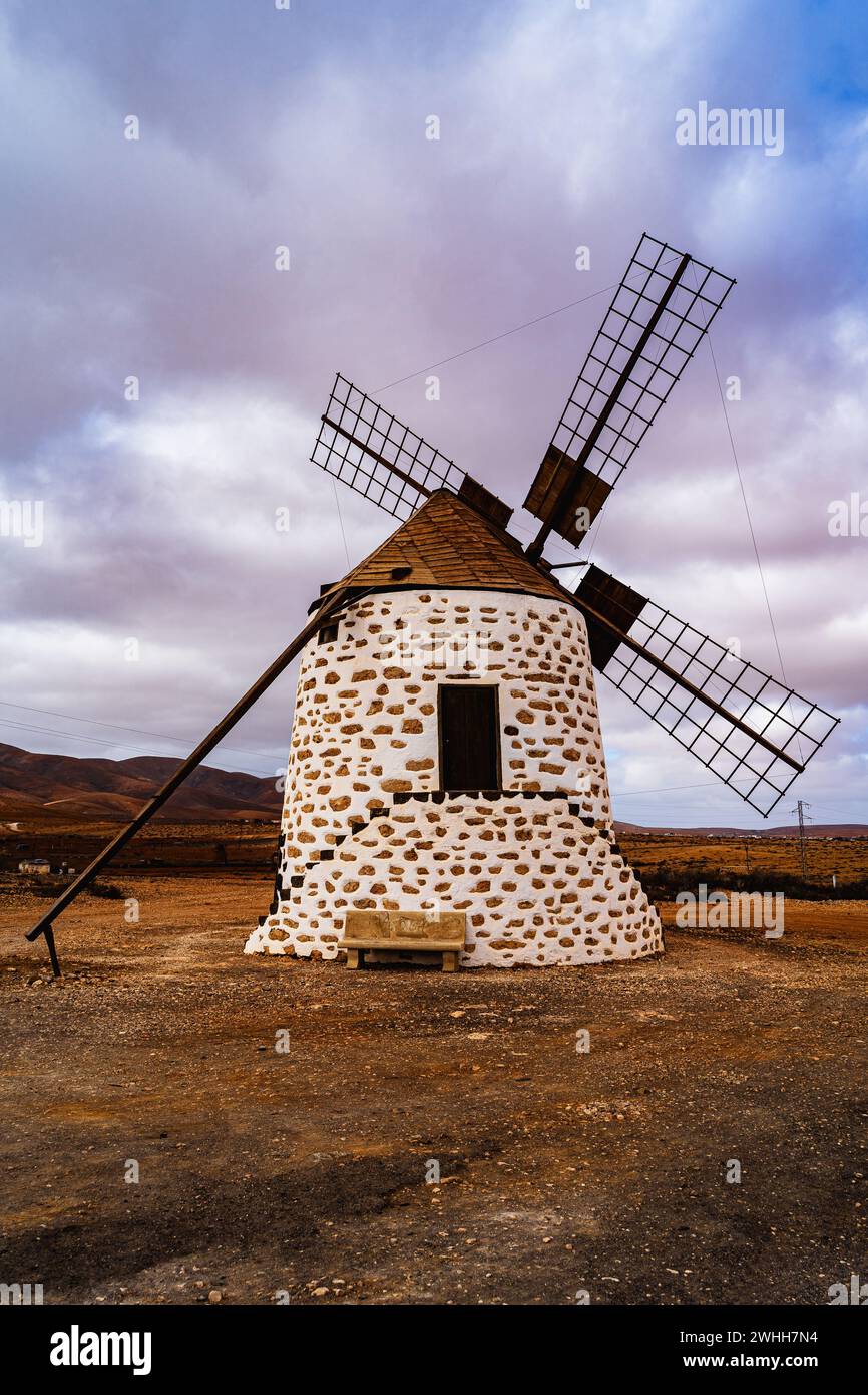 Eine traditionelle Windmühle steht allein inmitten einer kargen Landschaft unter einem bewölkten Himmel. Stockfoto